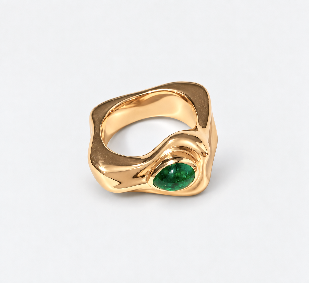 A gold ring with an organic, wavy shape and a green oval gemstone, photographed on a light gray background.