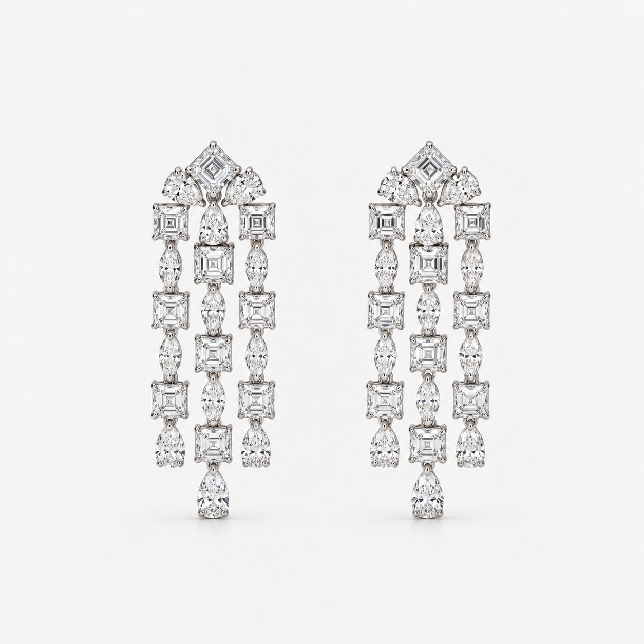A pair of long, dangling statement earrings featuring multiple columns of diamonds in square, baguette, and pear shapes, set in a silver-toned metal against a light gray background.