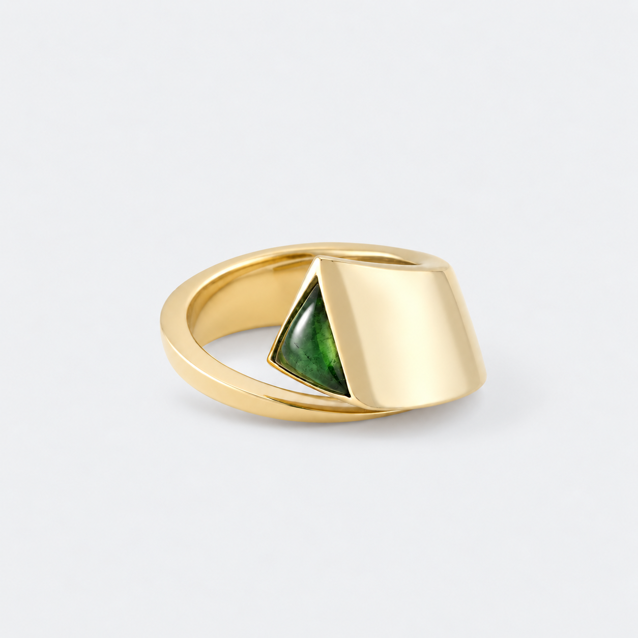 A gold ring with a geometric, wrap-around design and a triangular green stone inlay, shown on a light gray background.