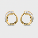 A pair of gold huggie hoop earrings with baguette-cut diamonds set along the front, shown on a light gray background.
