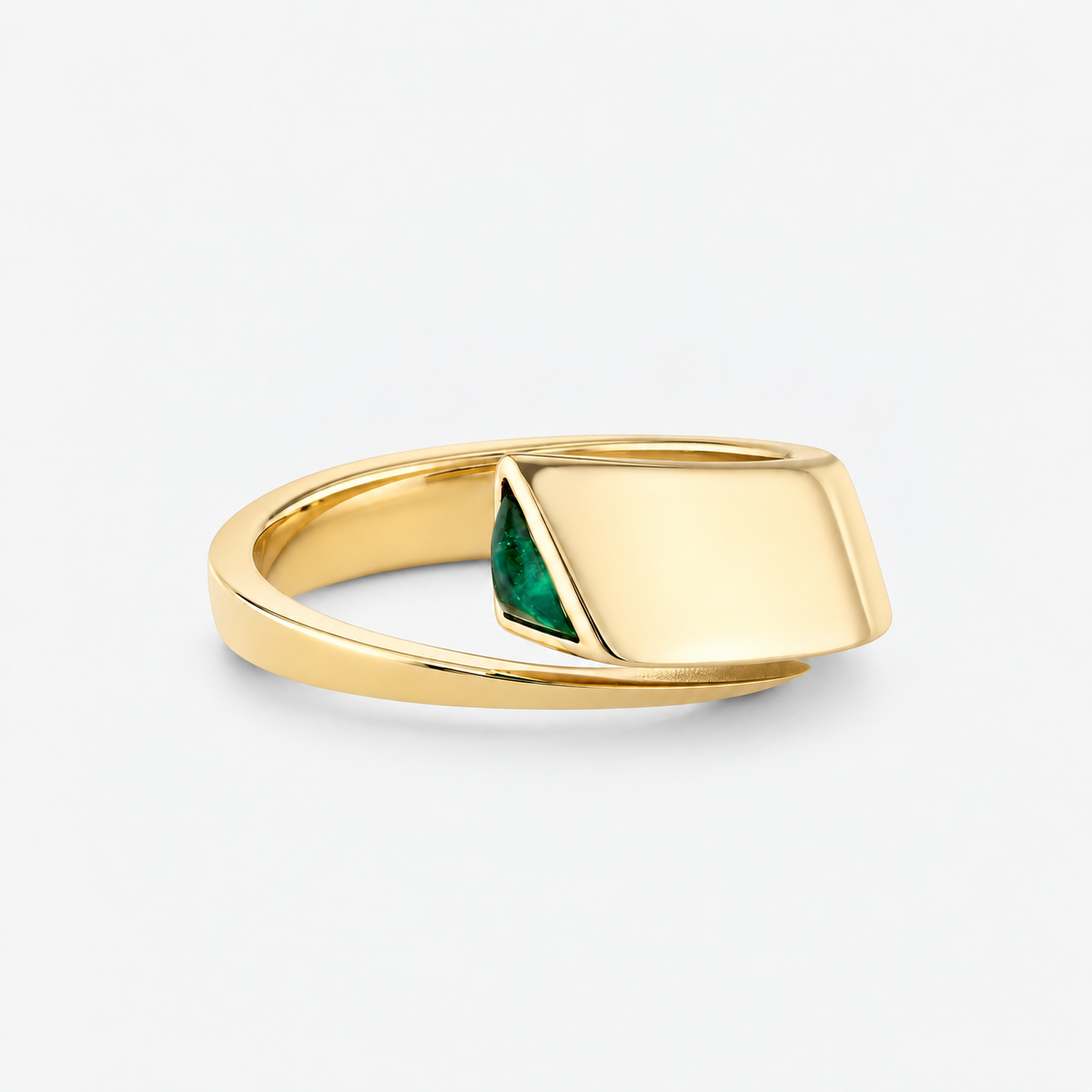 A gold signet-style ring with a flat rectangular face and a small triangular green stone inset, shown on a clean light gray background.