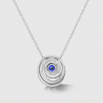 A white gold pendant necklace featuring a central round blue gemstone, displayed on a light gray background.