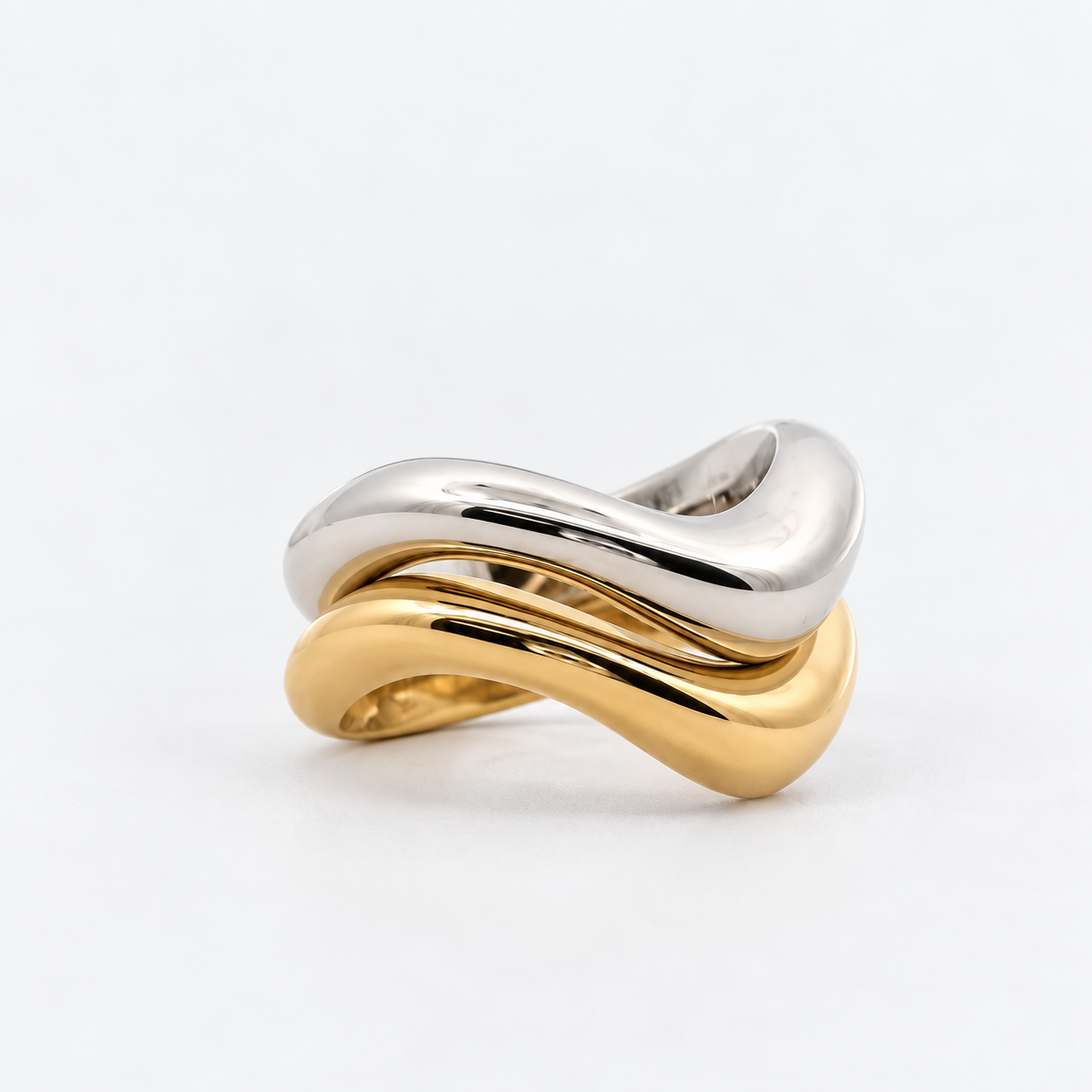 A two-tone wavy twist ring featuring polished silver and yellow gold metal bands, photographed on a clean white background.