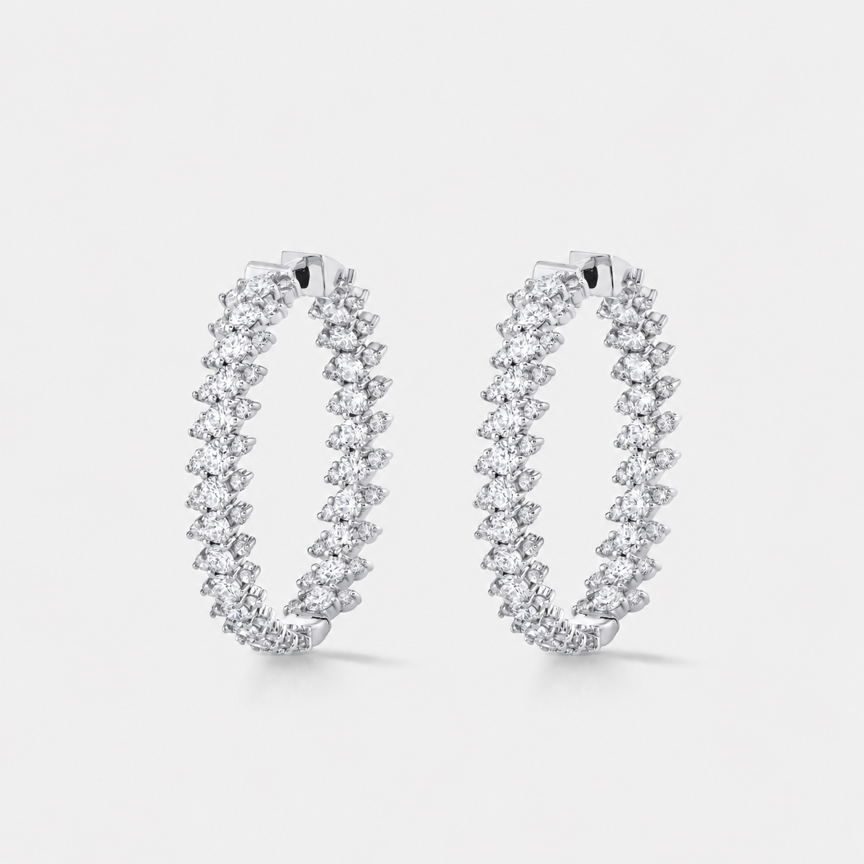 A pair of silver hoop earrings adorned with rows of round-cut diamonds, set against a clean light gray background.