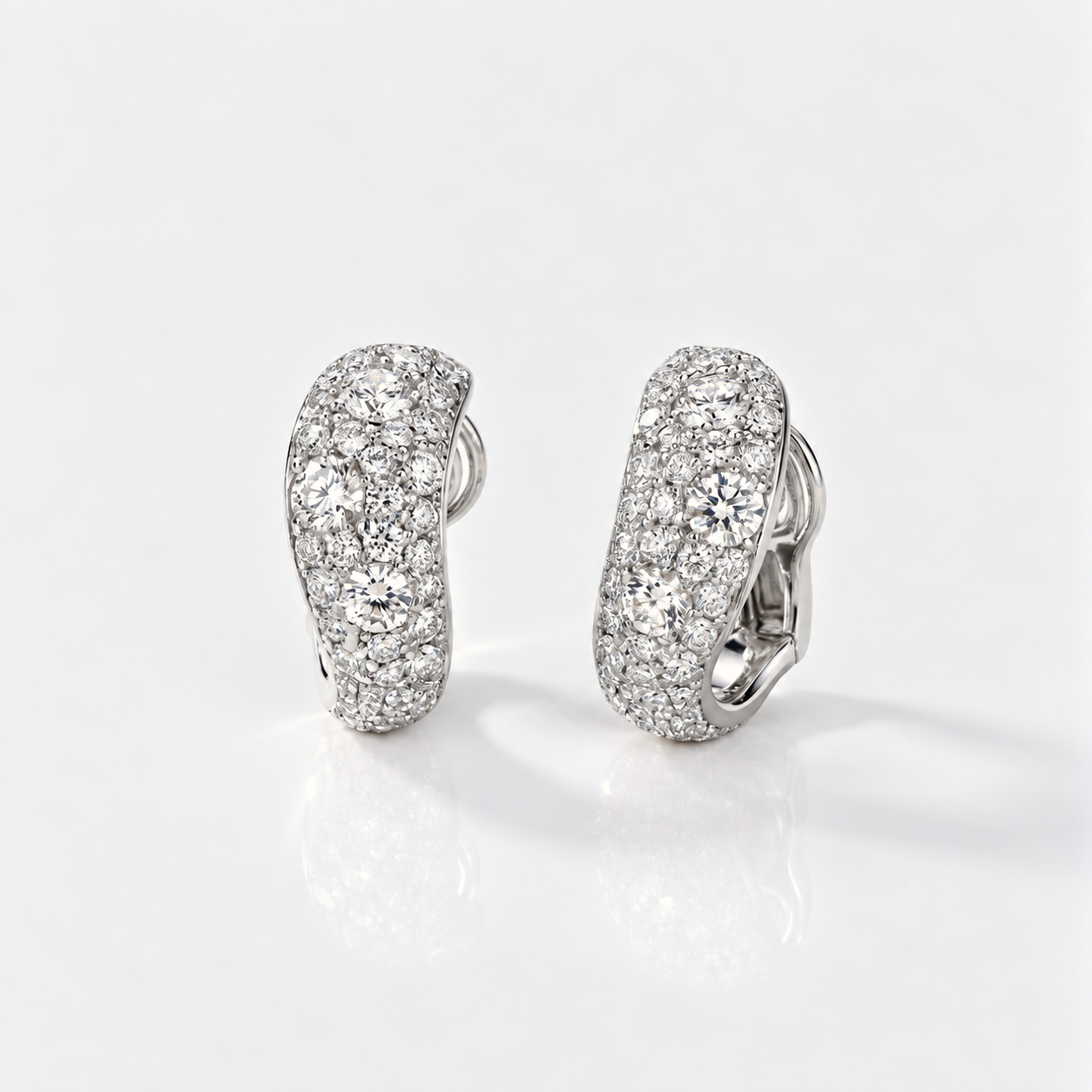 A pair of pavé-set hoop earrings in a silver-toned metal, covered with clear stones, displayed on a clean white reflective surface.