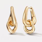 A pair of gold-toned hoop earrings with a thick, abstract interlocking chain-link design, shown on a light gray background.