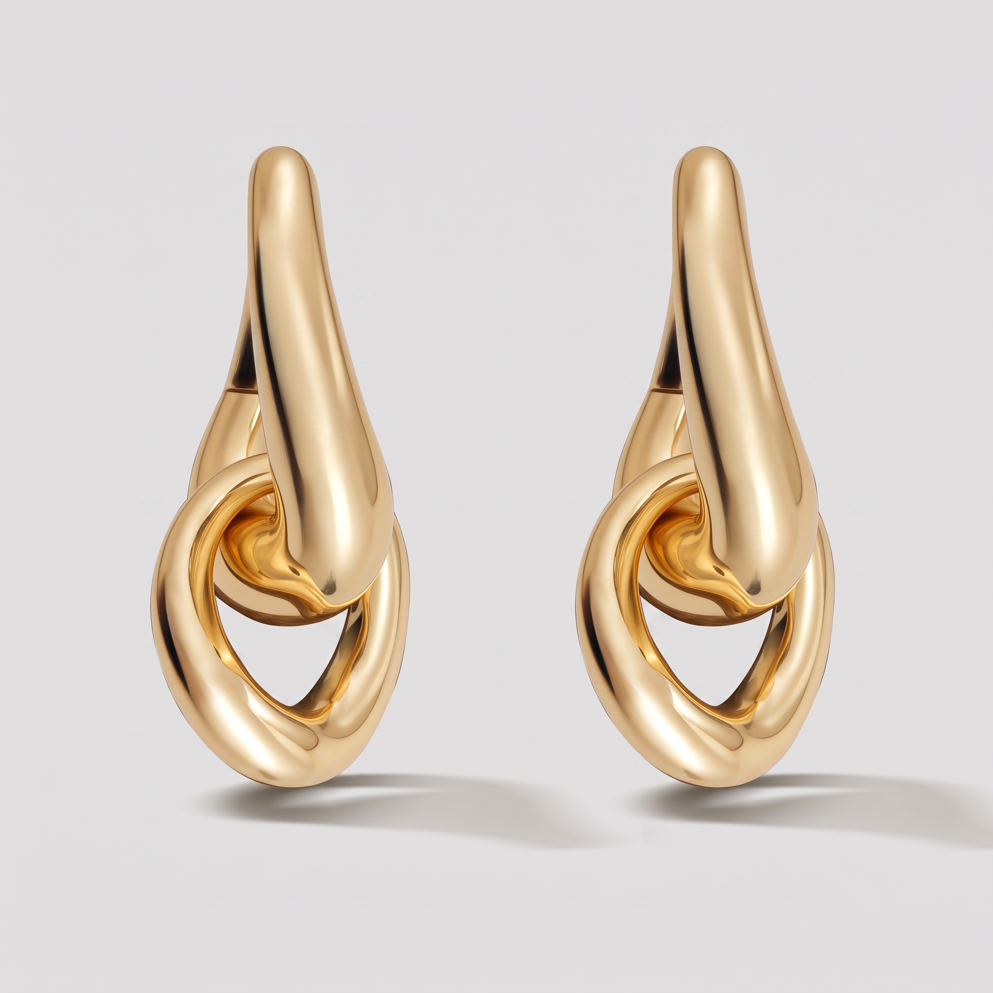 A pair of gold teardrop-shaped hoop earrings with an integrated interlocking ring design, shown on a light gray background.