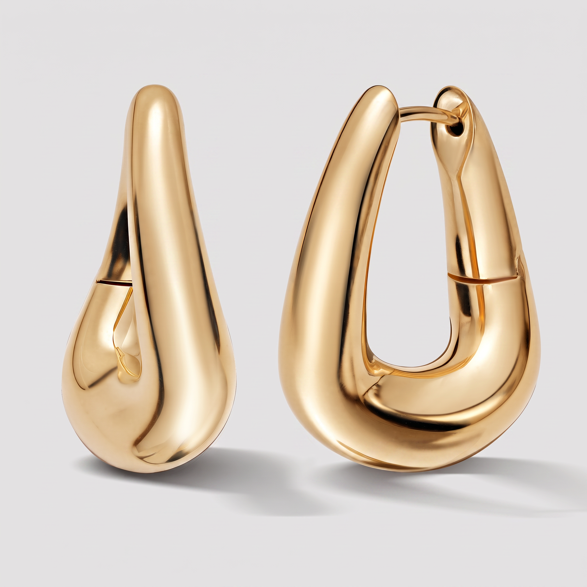 A pair of polished gold huggie hoop earrings with a teardrop-shaped organic design, shown on a light gray background.