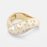 A gold ring with a wavy, organic shape, embellished with small and round clear diamonds, shown on a light gray background.