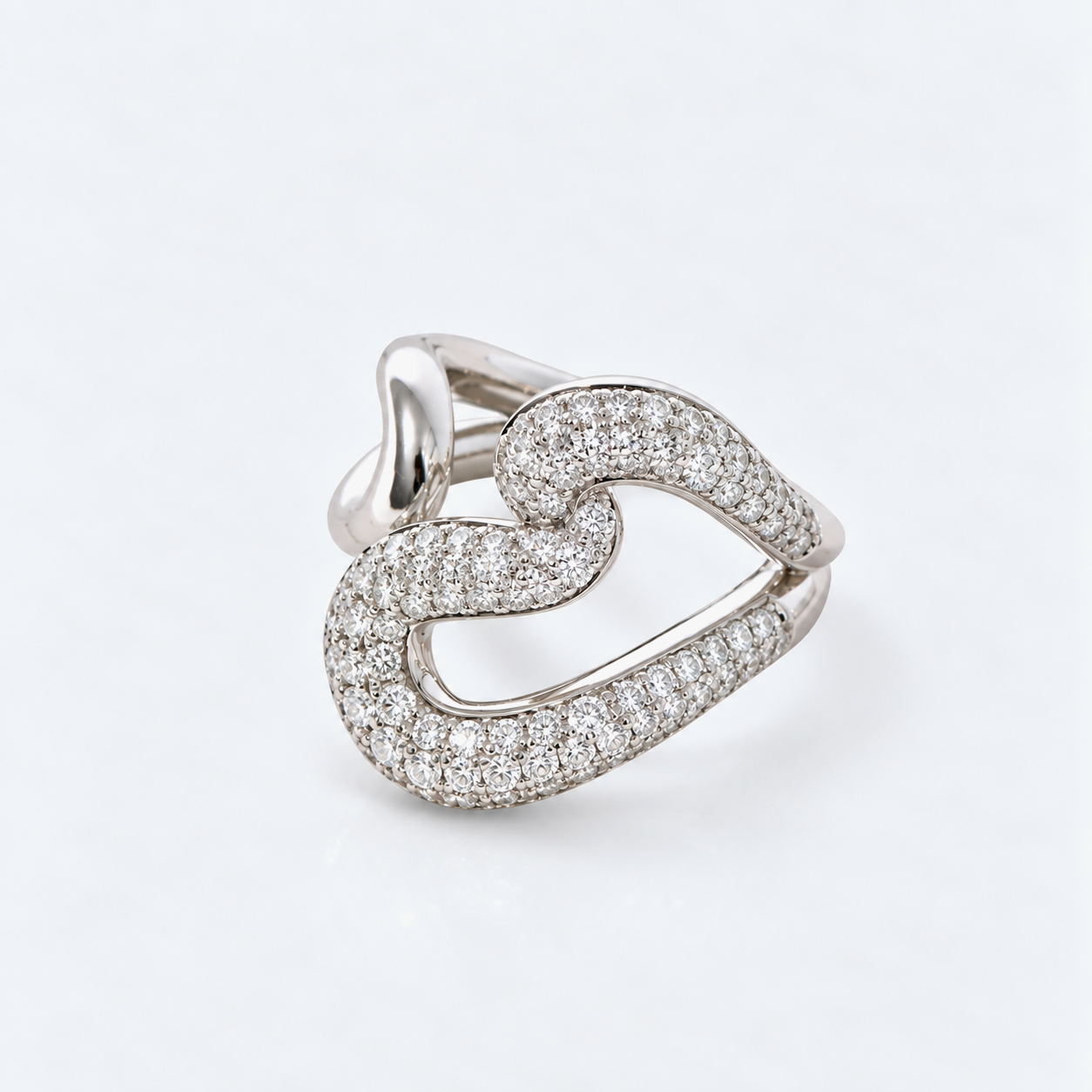 A silver-toned ring featuring an open, flowing heart-shaped design paved with small clear stones, photographed on a clean white background.