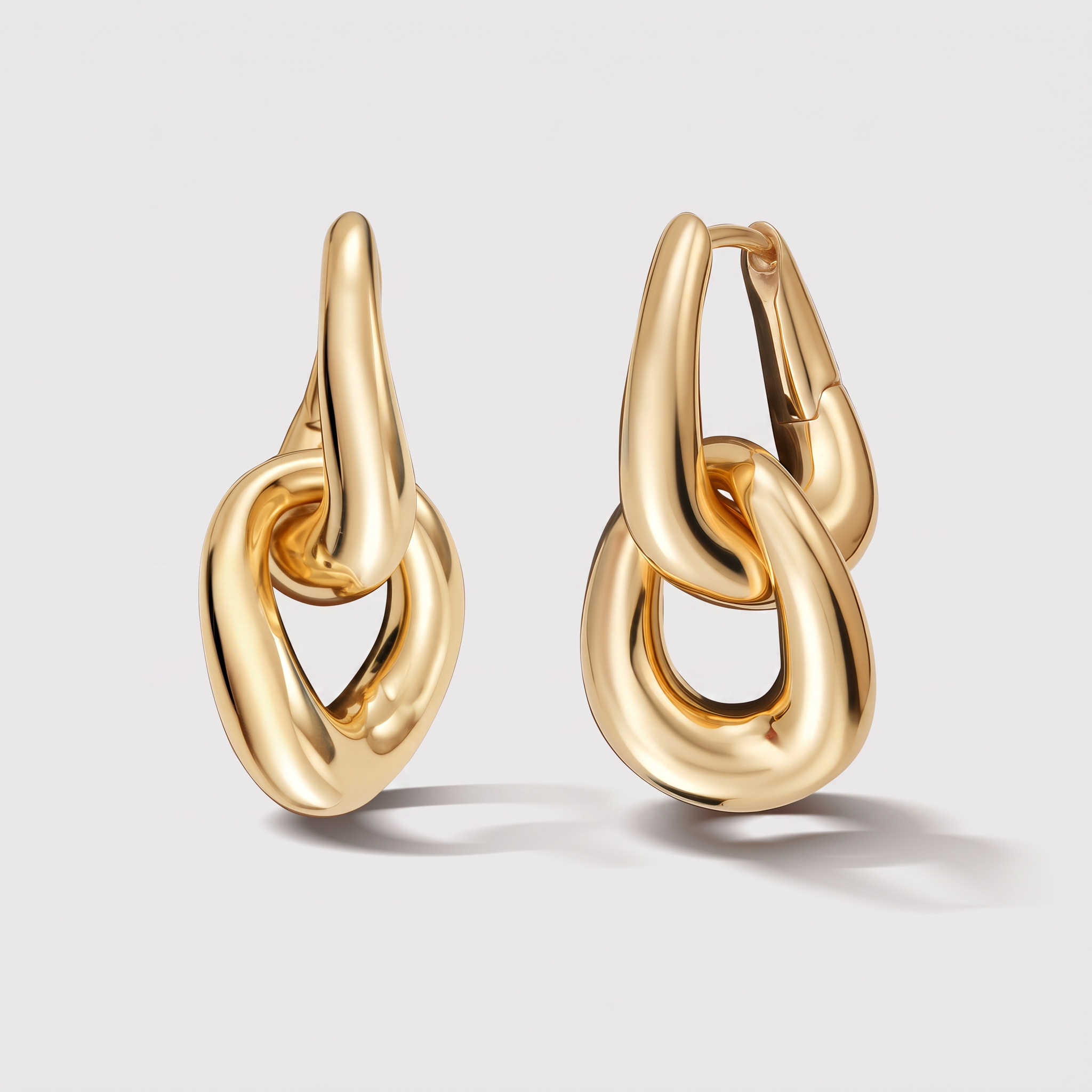 A pair of gold huggie hoop earrings with a thick, polished abstract knot design, shown on a light gray background.