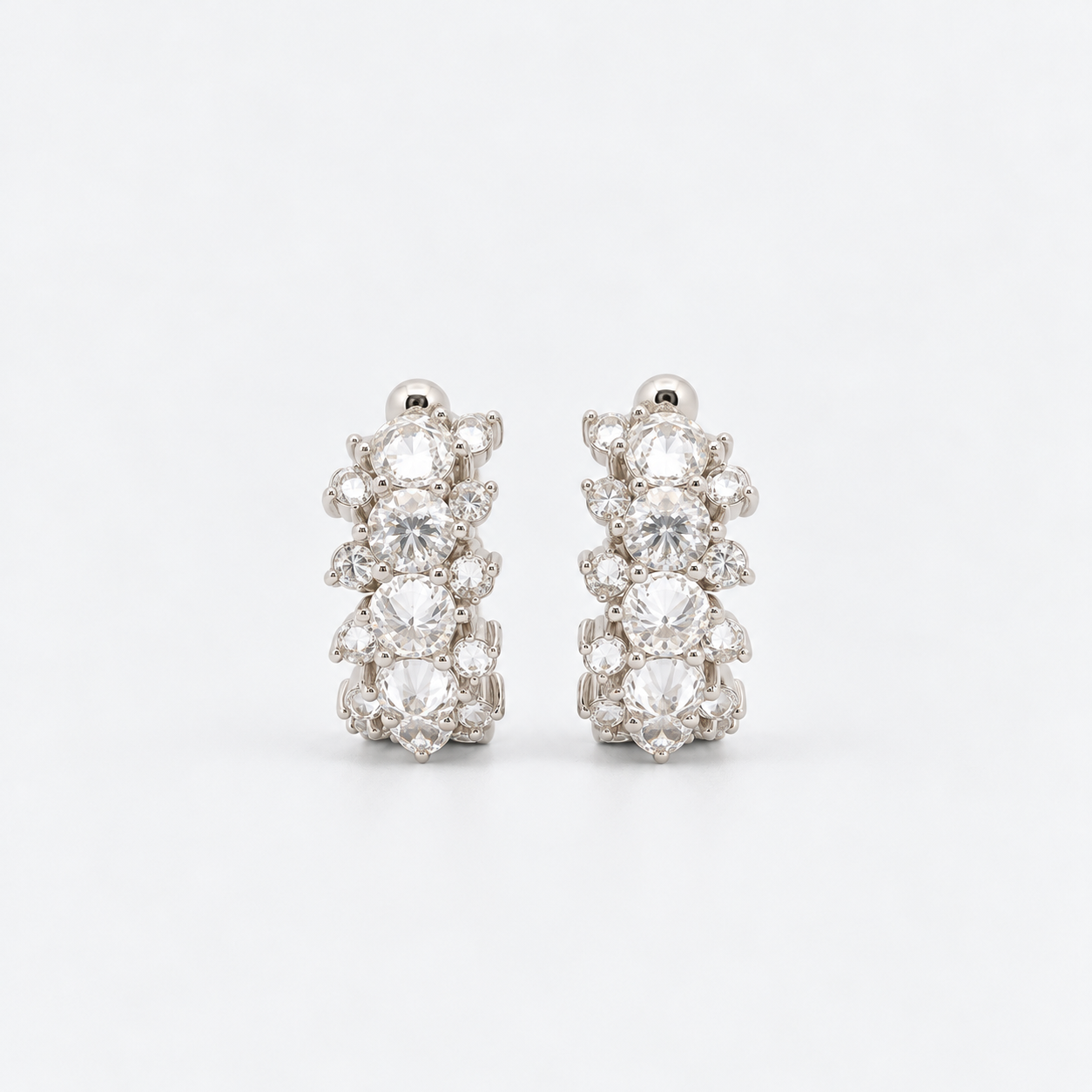 A pair of silver-toned huggie hoop earrings adorned with reverse set diamonds and round-cut diamonds, set against a clean white background.