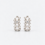 A pair of silver-toned huggie hoop earrings adorned with reverse set diamonds and round-cut diamonds, set against a clean white background.