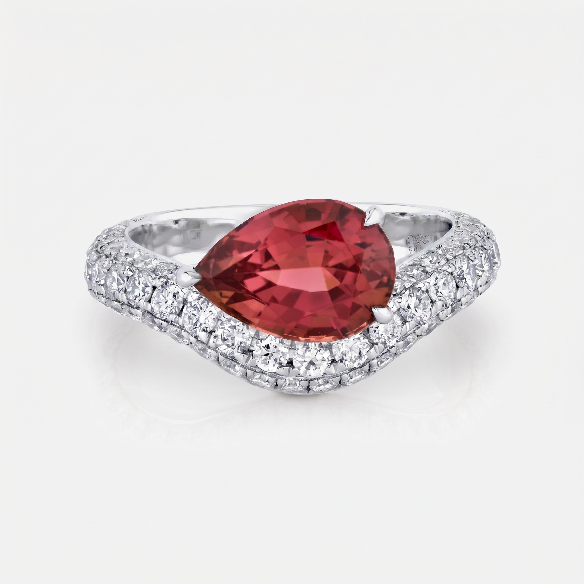 A pear-cut red gemstone ring set in a white gold pavé band, photographed on a clean white background.