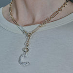 A close-up of a person wearing a multi-strand gold and silver chain necklace with a C initial charm, styled with a light gray t-shirt.
