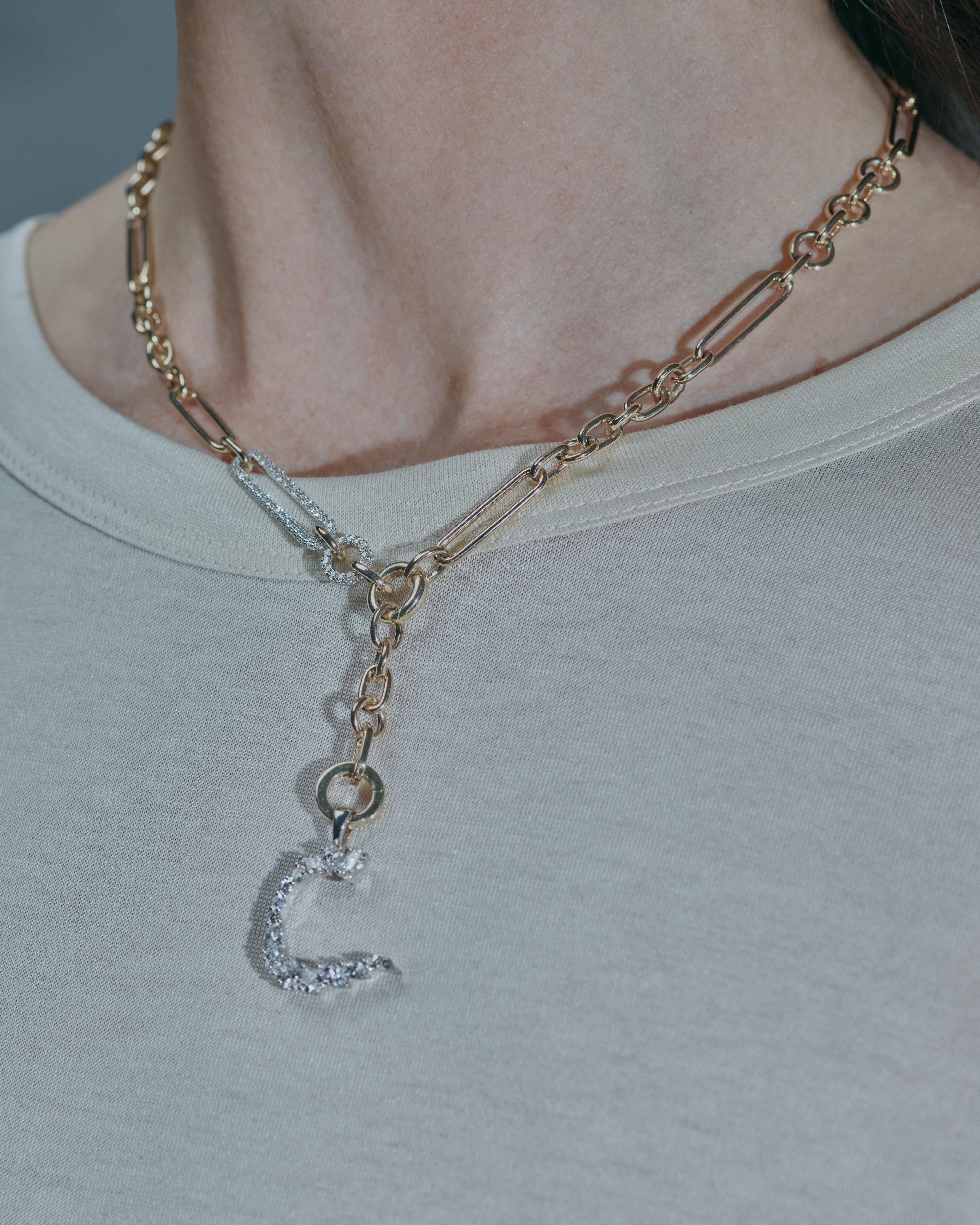A close-up of a person wearing a multi-strand gold and silver chain necklace with a C initial charm, styled with a light gray t-shirt.