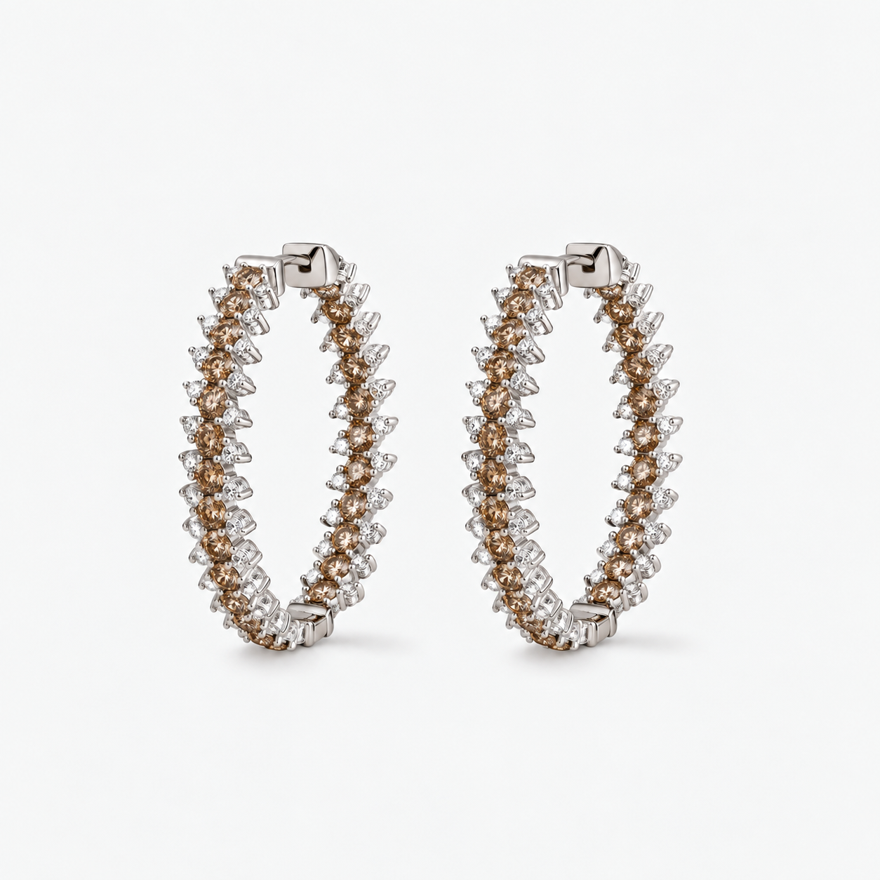 A pair of large hoop earrings with white and champagne diamonds set in polished white-toned metal. The earrings are displayed on a clean, light gray background.