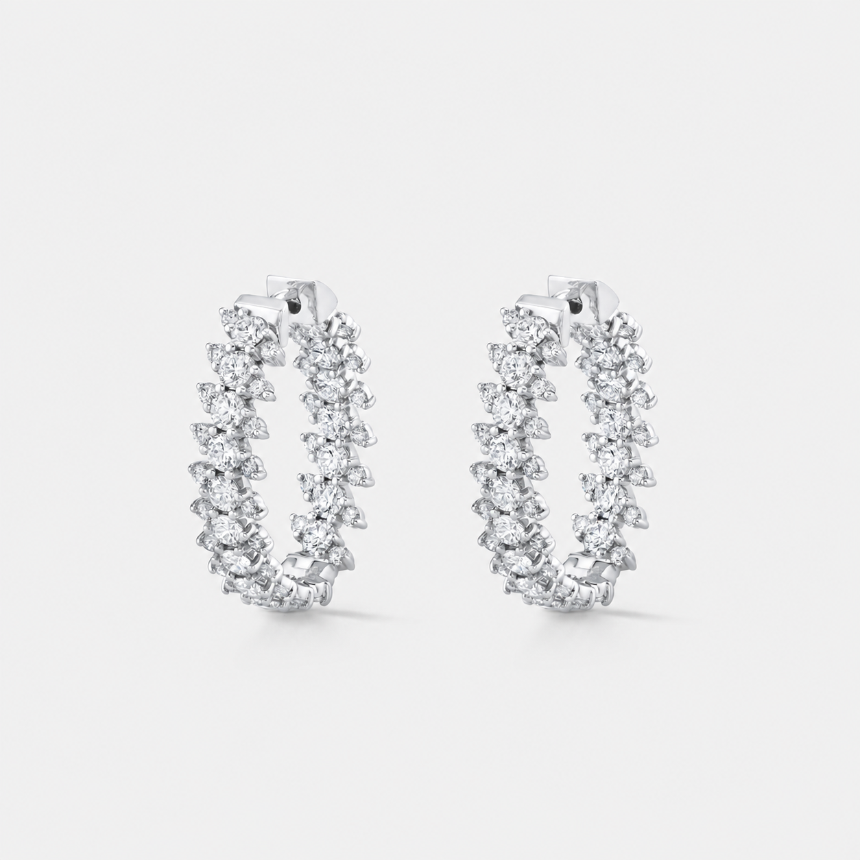A pair of silver-tone hoop earrings adorned with multiple rows of diamonds, set against a light gray background.