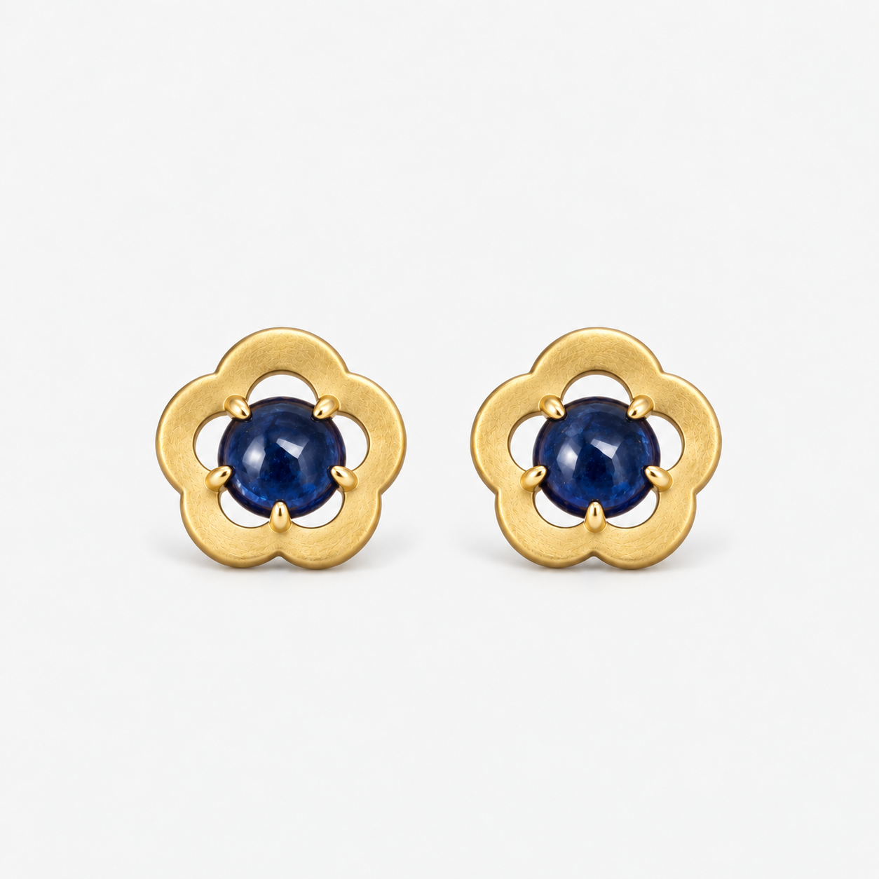 A pair of gold flower-shaped stud earrings with round sapphirescabochon gemstones in the center, set against a clean white background.