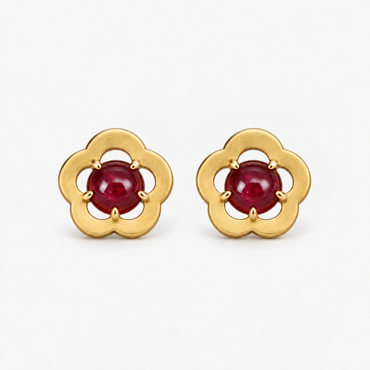 A pair of gold flower-shaped stud earrings with round red gemstones in the center, set against a clean white background.