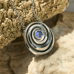 gold spiral pendant set with a tanzanite in the center designed by Isabel Delgado