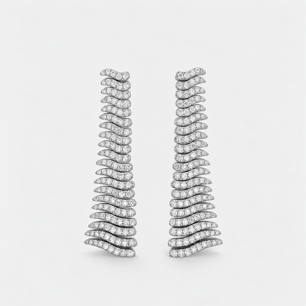 A pair of wavy, tiered drop earrings set with small diamonds in a silver-toned metal, displayed against a clean, light gray background.