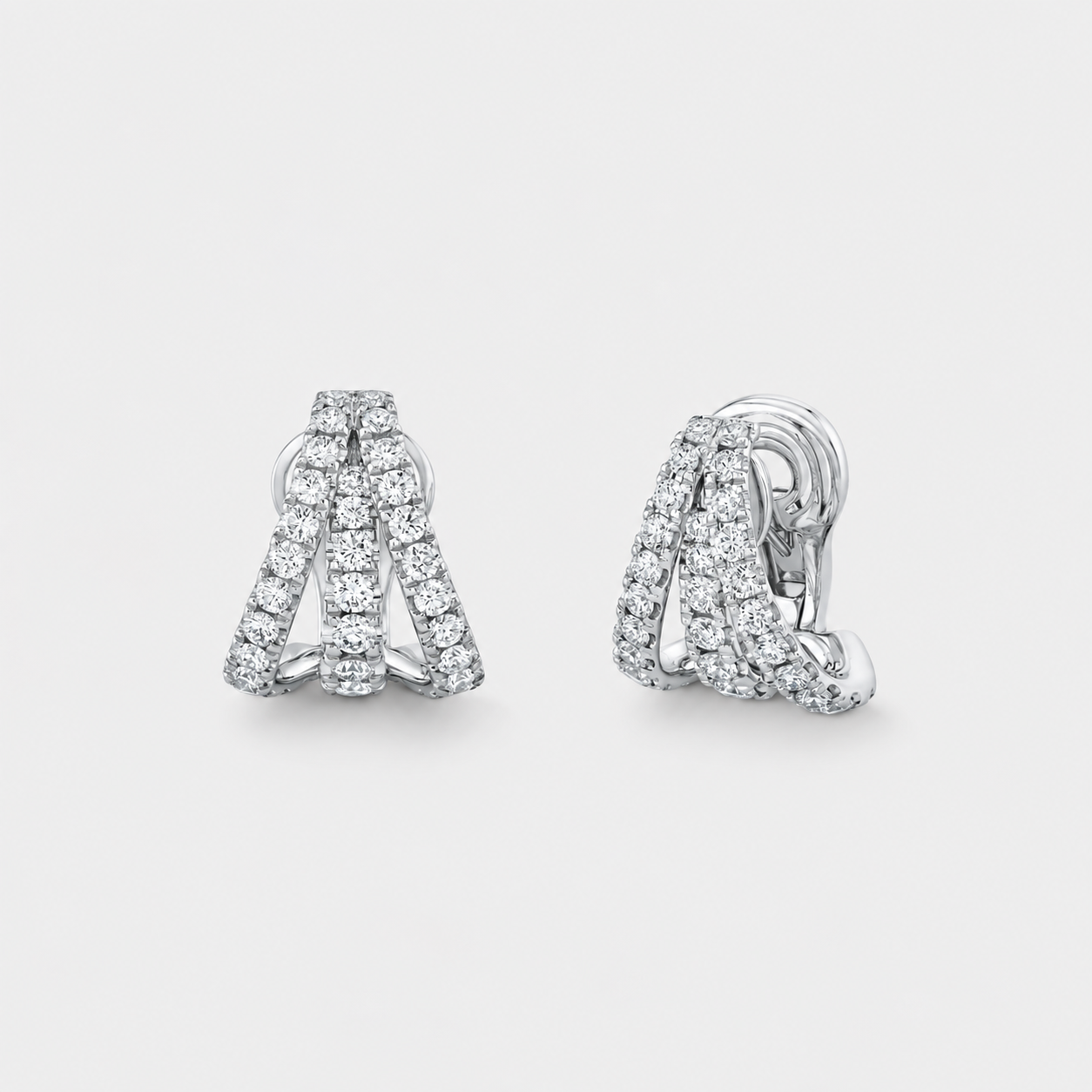 A pair of silver-toned huggie hoop earrings adorned with pavé-set clear diamonds, shown from the front and side on a light gray background.