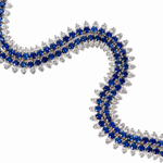A close-up of a luxury necklace featuring rows of deep blue round-cut gemstones and clear marquise-cut gemstones set in a white-toned metal, arranged in a flowing S-shape on a solid white background.