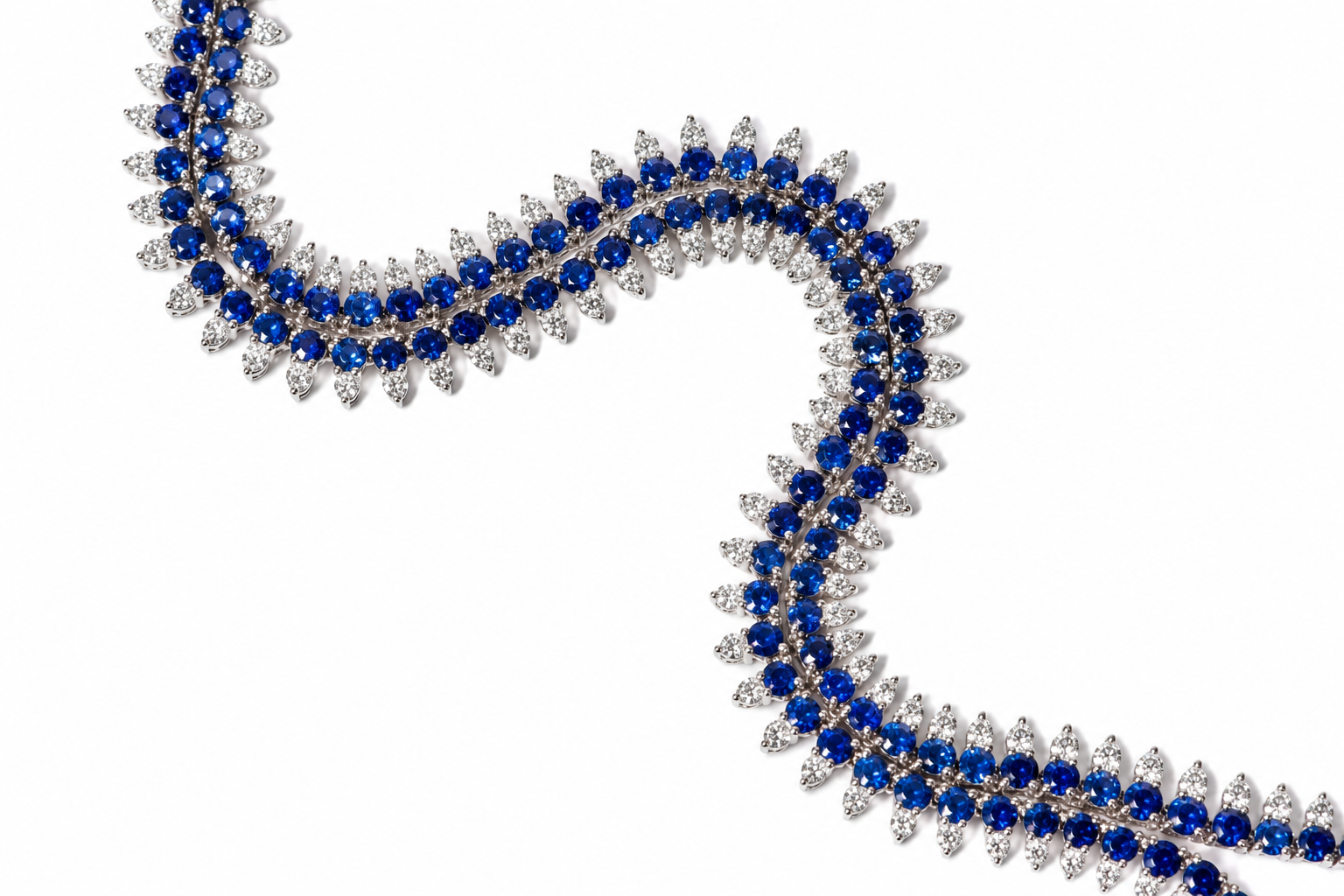 A close-up of a luxury necklace featuring rows of deep blue round-cut gemstones and clear marquise-cut gemstones set in a white-toned metal, arranged in a flowing S-shape on a solid white background.