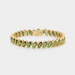 A gold tennis bracelet featuring marquise-cut green tourmalines, displayed on a clean light gray background.