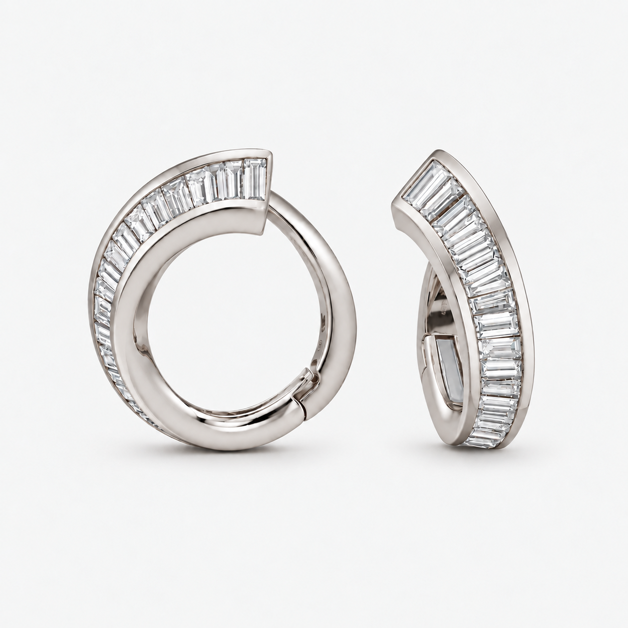 A pair of silver-toned huggie hoop earrings with baguette-cut clear diamonds, shown from two angles on a light gray background.