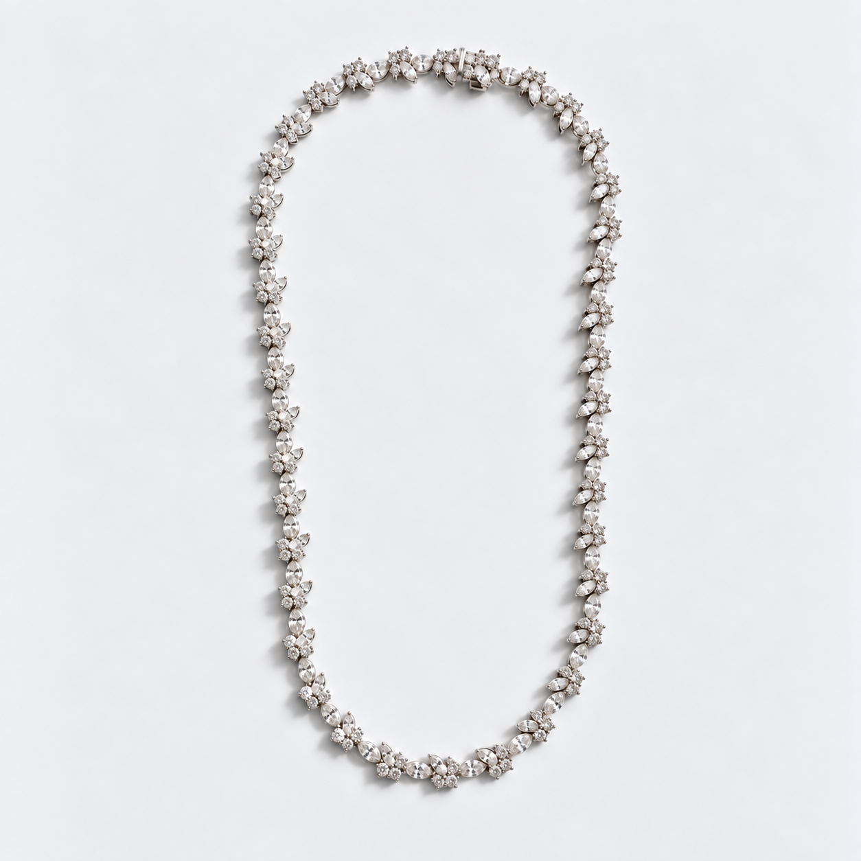 A delicate silver-toned necklace featuring a continuous line of small, flower-like clusters of clear gemstones, laid flat on a clean white background.