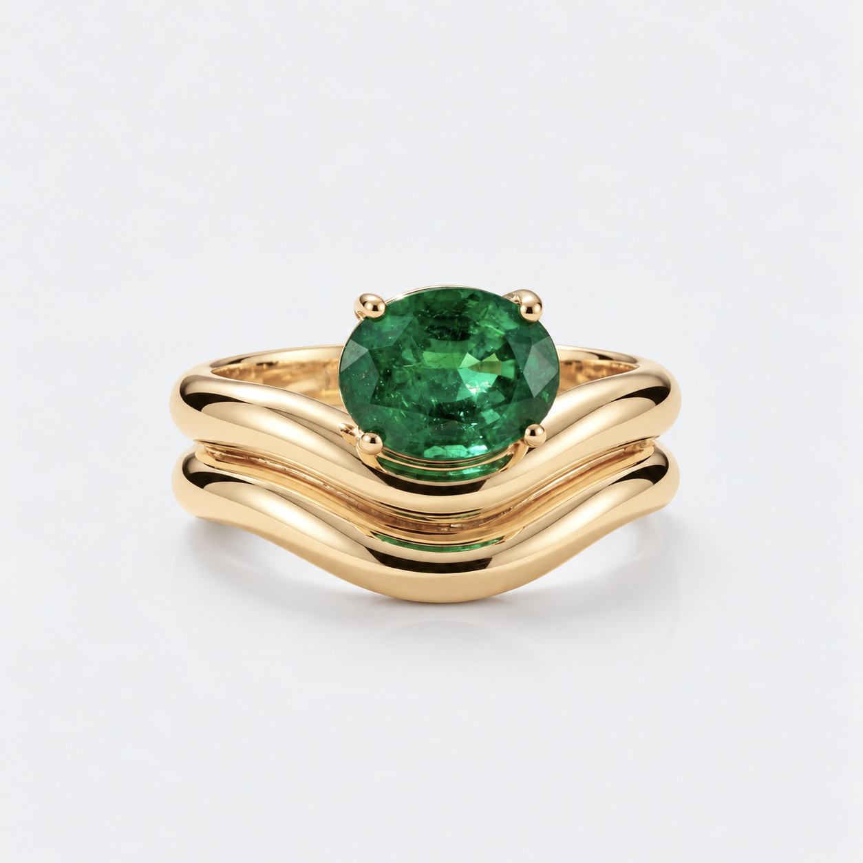 A gold ring with a wavy, layered band and a large oval-cut green emerald gemstone in the center, set against a clean white background.