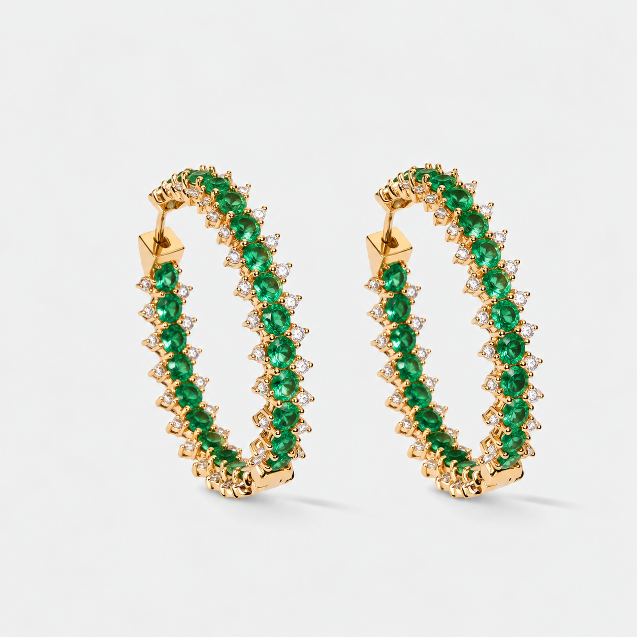 A pair of gold hoop earrings adorned with a double row of round-cut green emeralds and small diamonds, set against a clean white background.