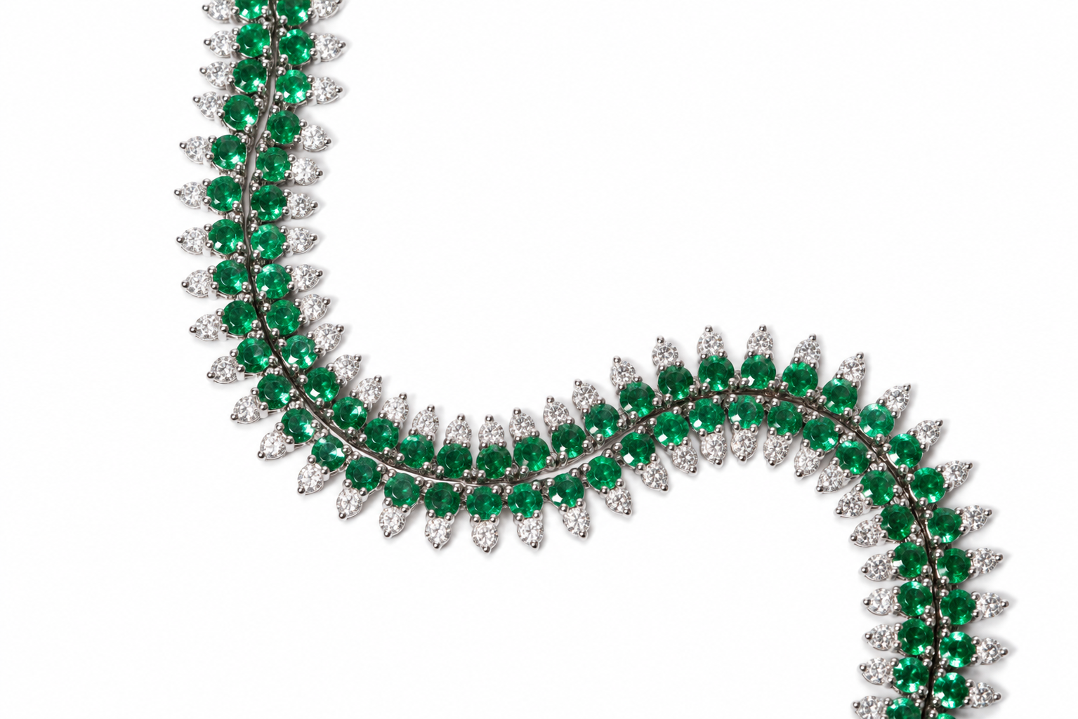 A close-up of a luxury necklace featuring rows of round-cut emerald green gemstones and pear-cut clear gemstones in a white-toned setting, arranged in a curved S-shape on a solid white background.