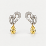 A pair of high-end diamond earrings featuring a pavé heart design in white metal with a dangling pear-cut yellow gemstone below, set against a clean white background.