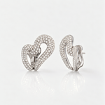 A pair of silver-toned heart-shaped earrings paved with small clear stones, shown from the front and side on a clean white reflective surface.