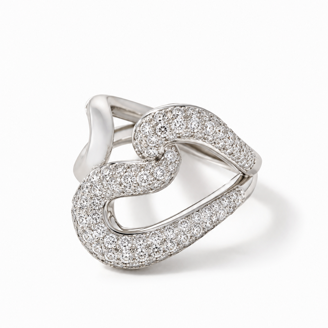 A silver-toned ring featuring an open, flowing heart-shaped design paved with clear stones, shown on a clean white background.