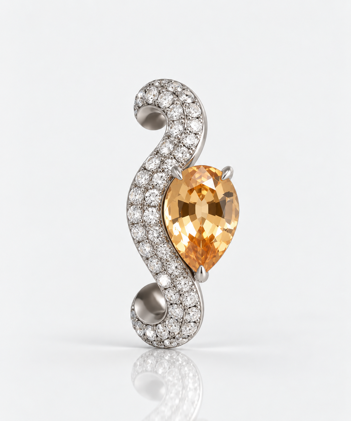 A curved silver-tone jewelry piece featuring a pear-cut orange gemstone in a prong setting, surrounded by pavé-set clear stones, photographed on a clean light gray background with a soft reflection below.