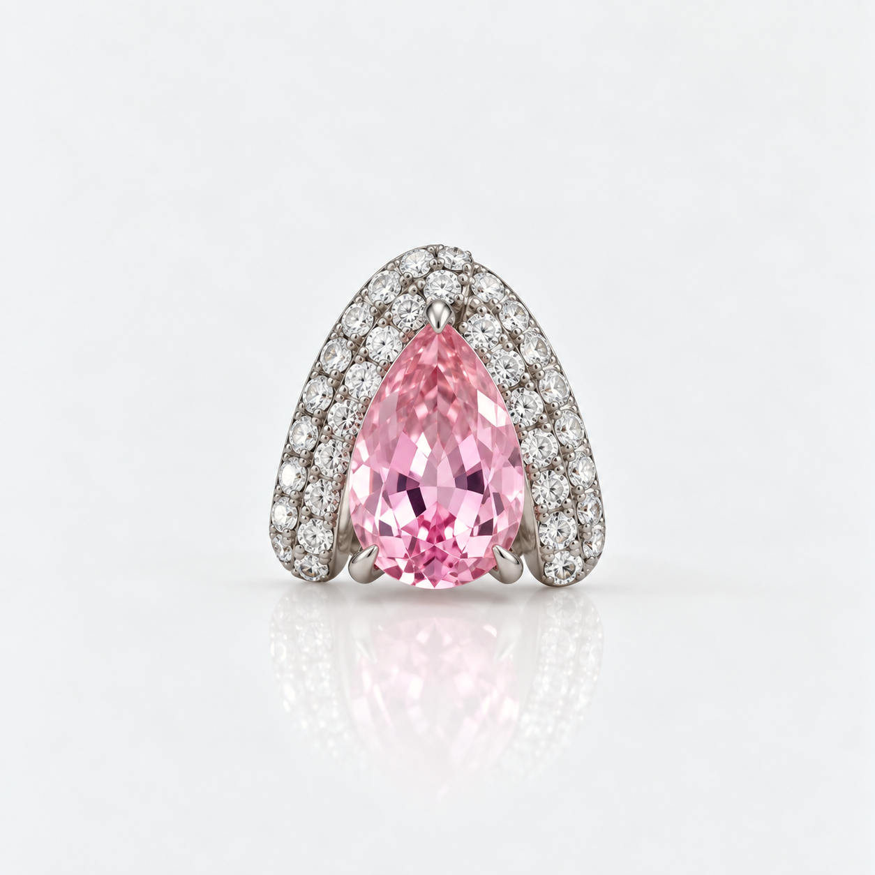 A pear-cut pink gemstone ring set in a silver-toned pavé band, photographed on a clean white reflective surface.