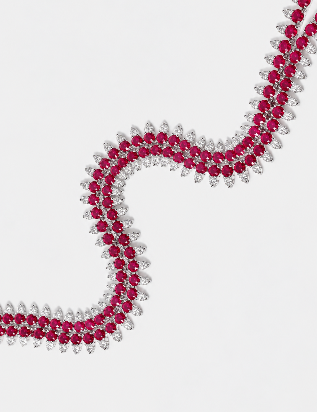 A close-up of a silver-toned necklace featuring rows of round deep pinkish-red rubies and round diamonds, arranged in a flowing S-shape on a light gray background.