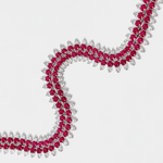 A close-up of a silver-toned necklace featuring rows of round deep pinkish-red rubies and round diamonds, arranged in a flowing S-shape on a light gray background.