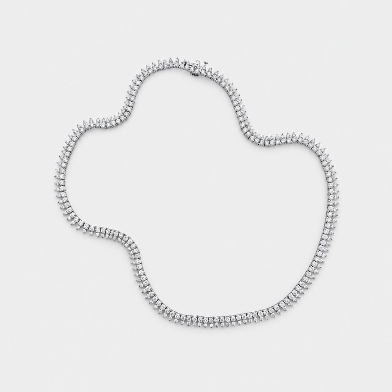 A silver tennis-style necklace with diamonds arranged in an irregular shape on a light gray background.