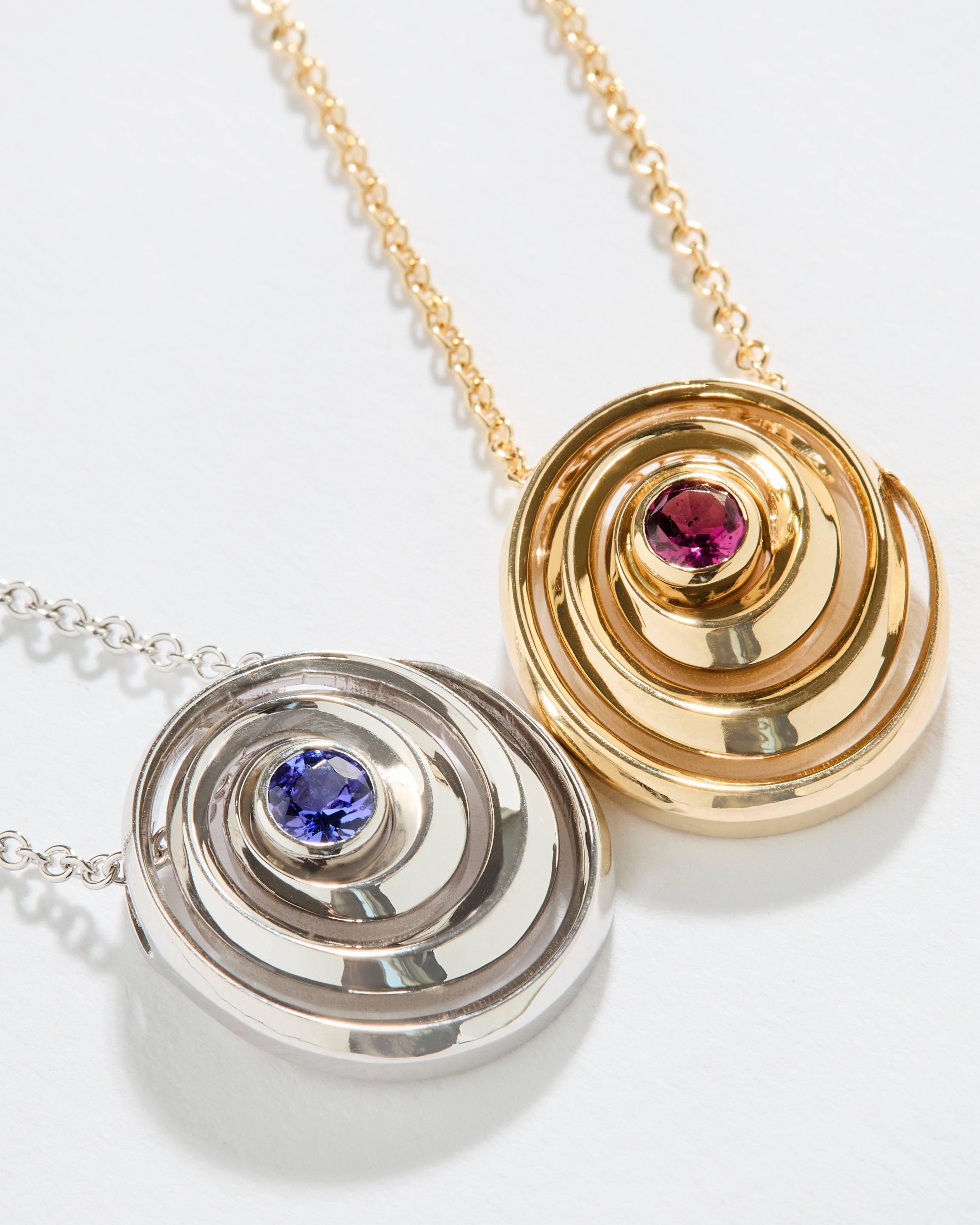gold spiral pendant set with a tanzanite in the center designed by Isabel Delgado alongside a pink tourmaline version of the same pendant